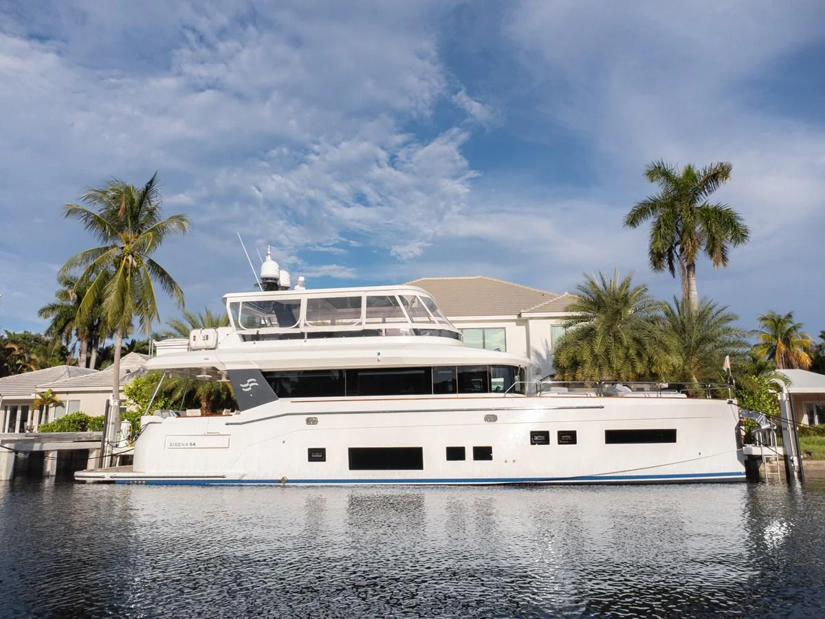 A sleek and modern yacht is docked by a waterfront property, showcasing its elegant design and spacious upper deck. aboard FANTASEA Yacht for Sale