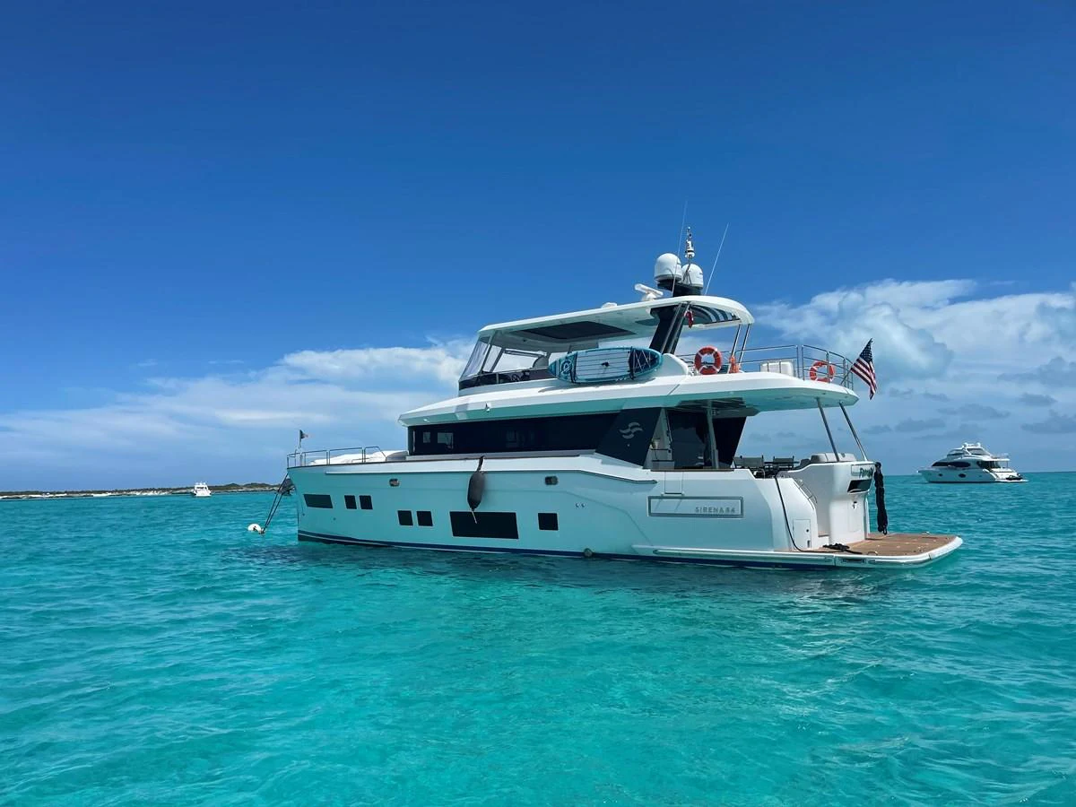 A sleek yacht is anchored in crystal-clear turquoise waters under a bright blue sky. aboard FANTASEA Yacht for Sale