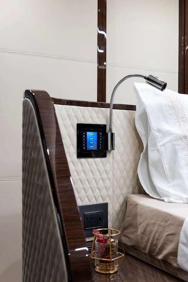 A luxurious bedside area featuring a quilted headboard, modern reading light, and integrated control panel. aboard NEW BUILD Yacht for Sale