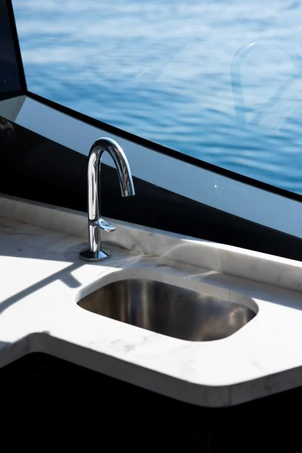 A sleek, modern sink with a chrome faucet is set against a backdrop of the sea through a large window. aboard NEW BUILD Yacht for Sale