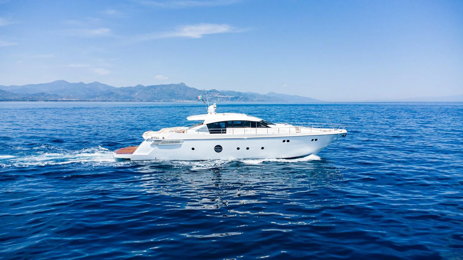A sleek white yacht cruises on calm blue waters with a scenic mountainous backdrop. aboard LUCHI Yacht for Sale