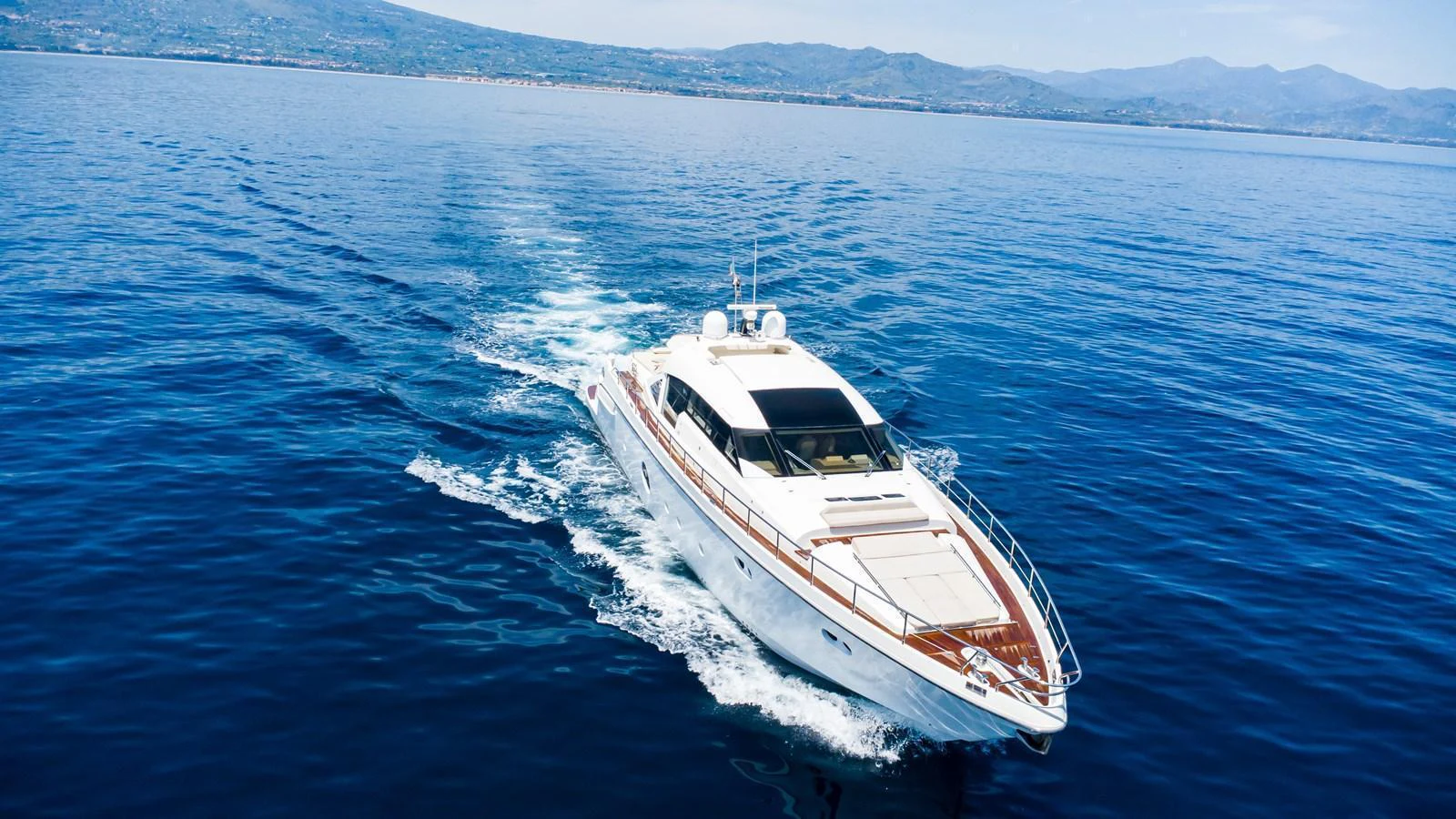 A sleek yacht cruises through calm blue waters with a scenic coastline in the background. aboard LUCHI Yacht for Sale