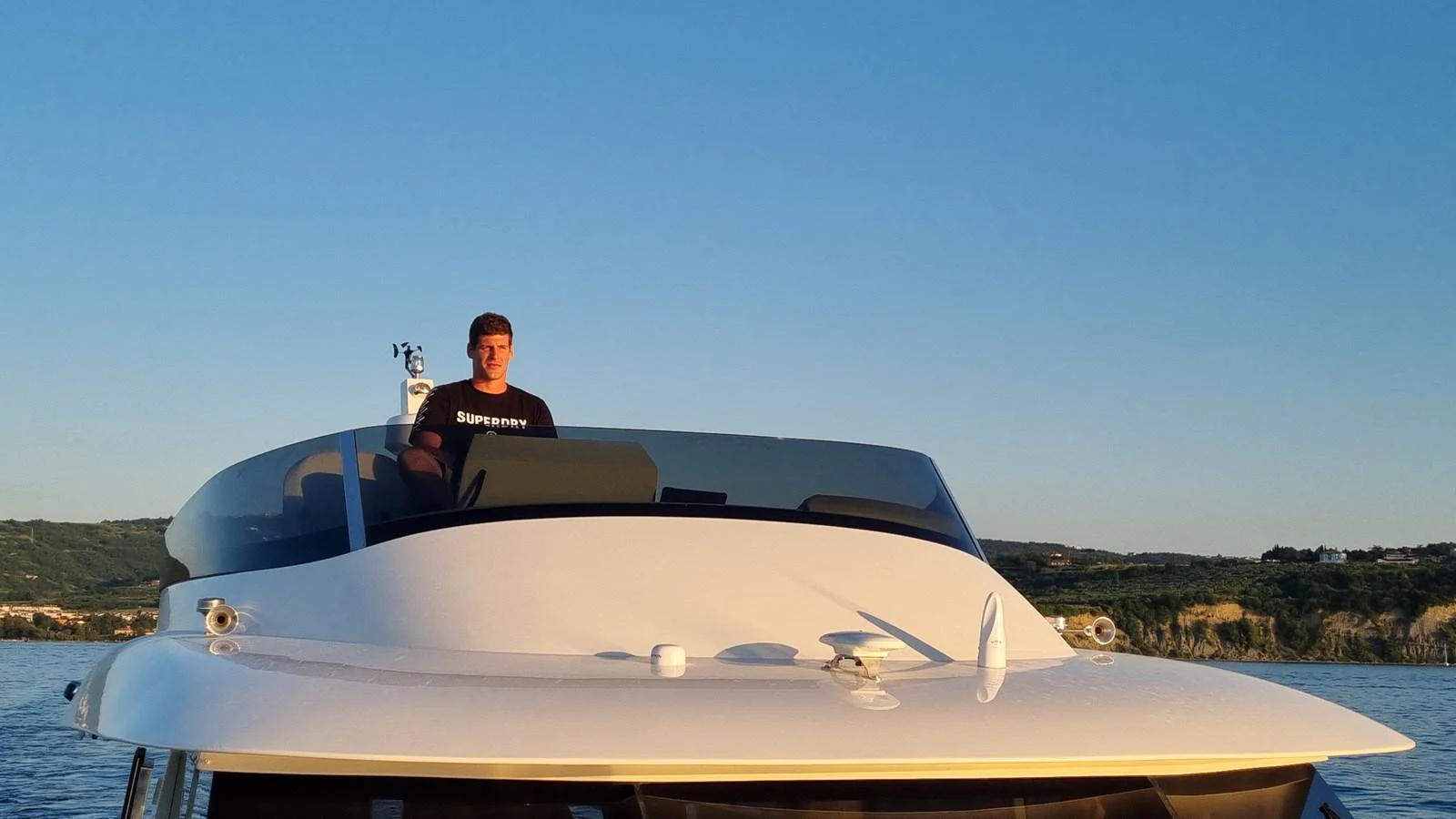A sleek yacht with a person standing on the upper deck, set against a scenic backdrop. aboard MONACHUS 70 FLY Yacht for Sale