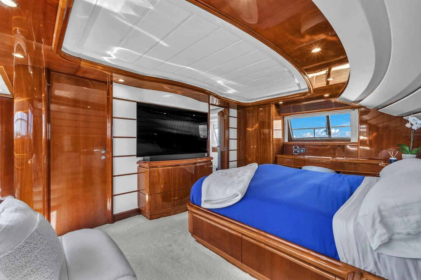 The master stateroom features luxurious wood paneling, a large bed with blue bedding, and a flat-screen TV. aboard FERRETTI YACHTS CUSTOM LINE 94 Yacht for Sale