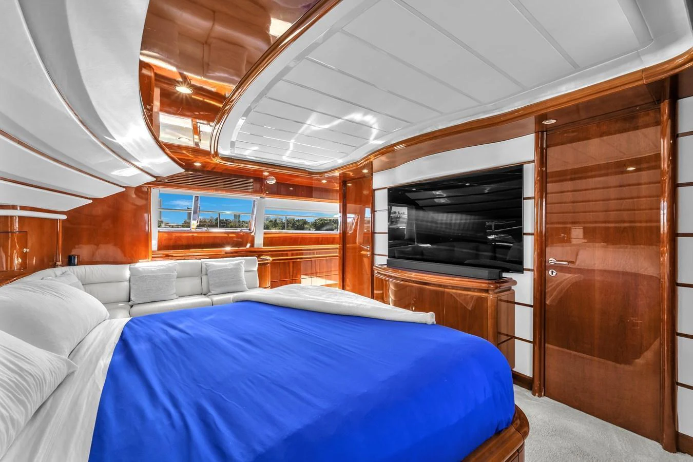 The luxurious stateroom features a plush bed with a vibrant blue cover, surrounded by rich wood paneling and ample natural light. aboard FERRETTI YACHTS CUSTOM LINE 94 Yacht for Sale
