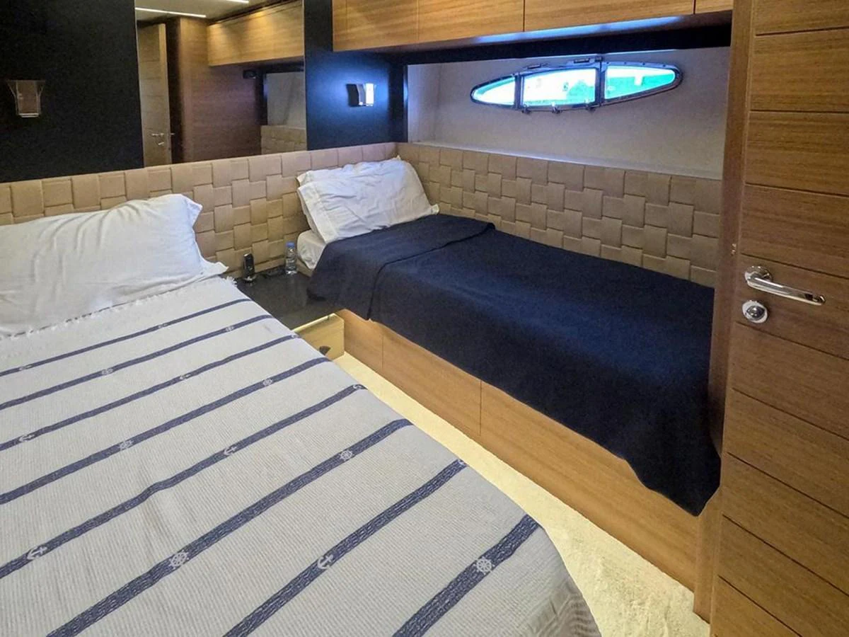 The guest stateroom features cozy twin beds with a modern design and a small porthole for natural light. aboard HONEY BADGER Yacht for Sale