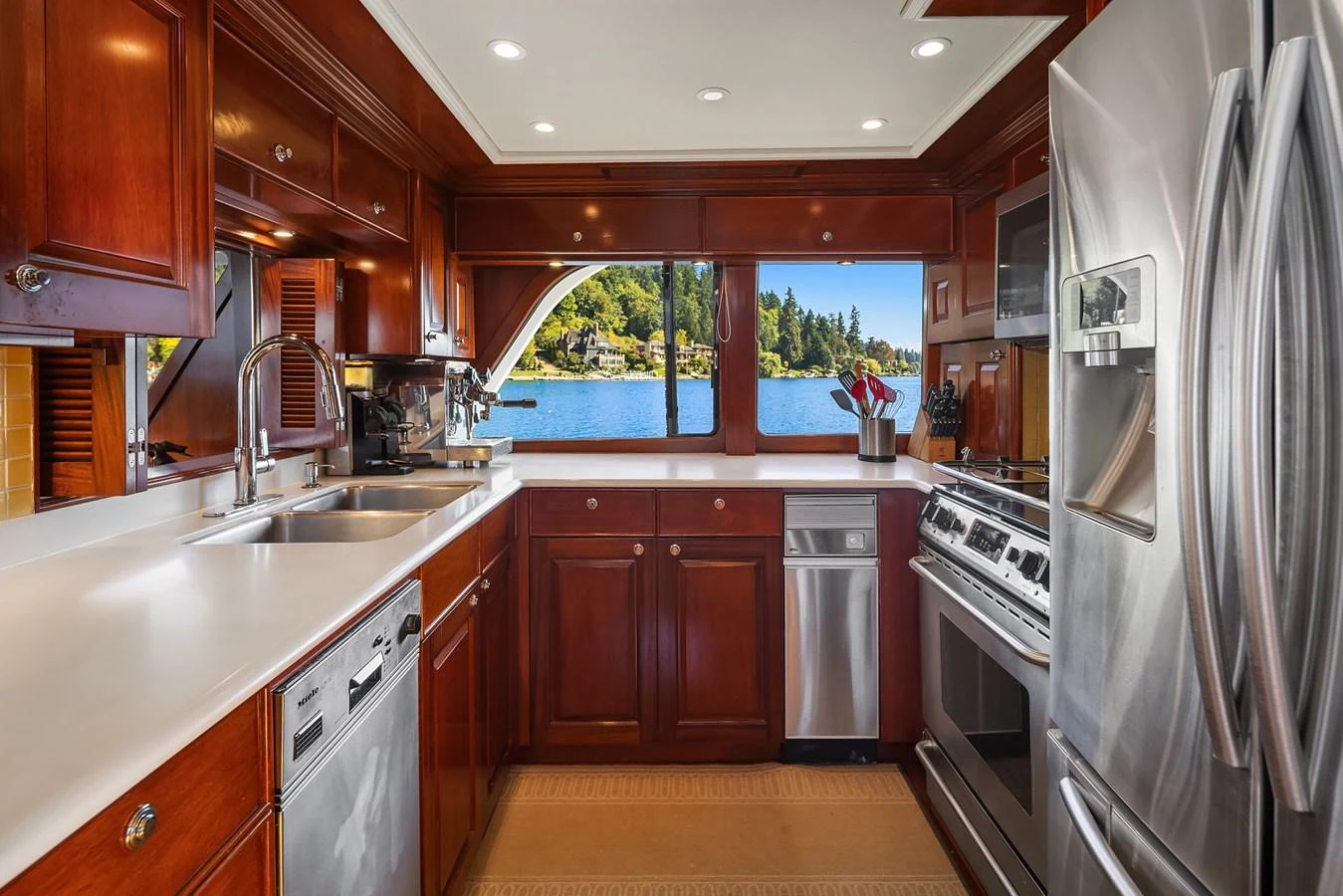 The yacht's galley features modern stainless steel appliances and rich wooden cabinetry, with a scenic view through the window. aboard MI AMERE Yacht for Sale