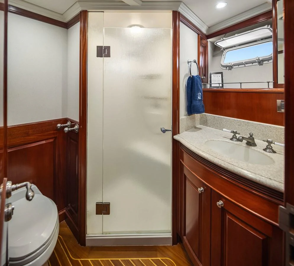 The yacht's bathroom features elegant wood cabinetry, a spacious countertop, and a glass-enclosed shower. aboard MI AMERE Yacht for Sale