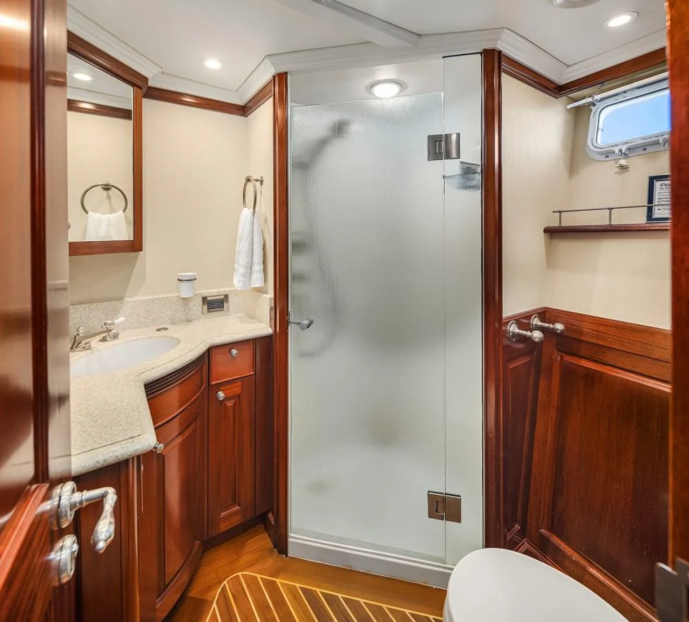 The yacht's bathroom features elegant wood cabinetry, a glass-enclosed shower, and modern fixtures. aboard MI AMERE Yacht for Sale
