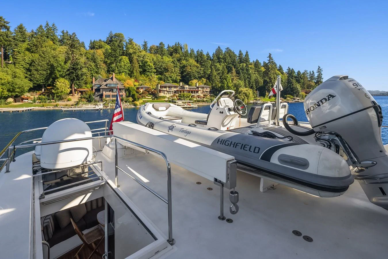 The yacht's deck features a high-quality tender and a scenic backdrop of lush greenery and waterfront properties. aboard MI AMERE Yacht for Sale