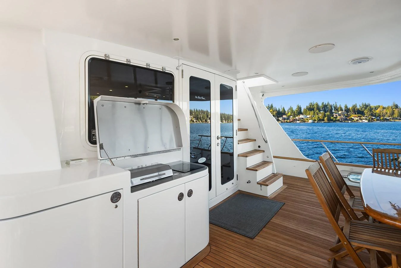 The aft deck features a dining area with wooden chairs and a built-in grill, offering a perfect spot for alfresco dining with a view of the water. aboard MI AMERE Yacht for Sale