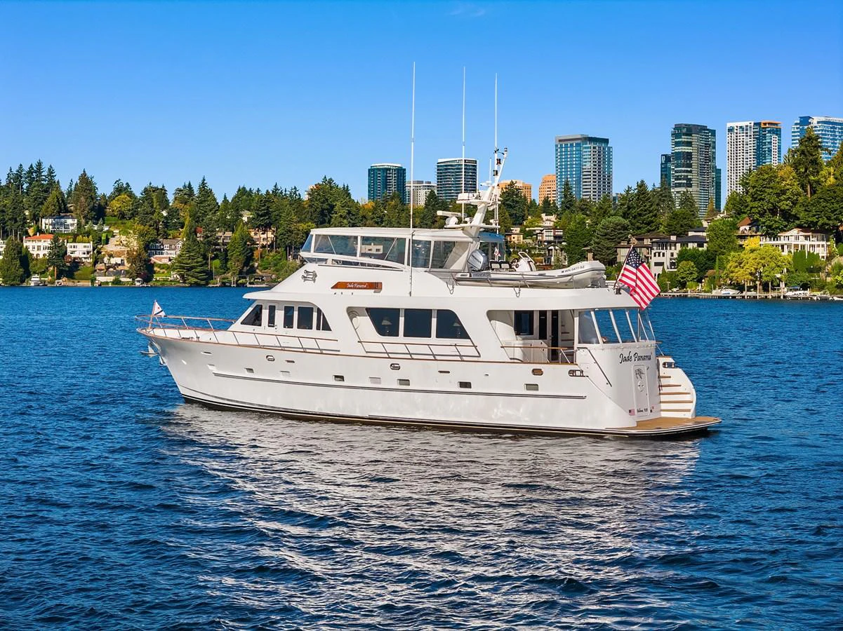 A luxurious yacht cruises gracefully on calm waters with a cityscape in the background. aboard MI AMERE Yacht for Sale