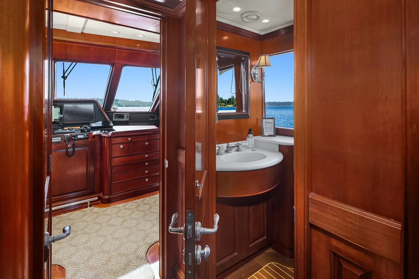 The image showcases a luxurious helm station with rich wood finishes and a compact bathroom area. aboard MI AMERE Yacht for Sale