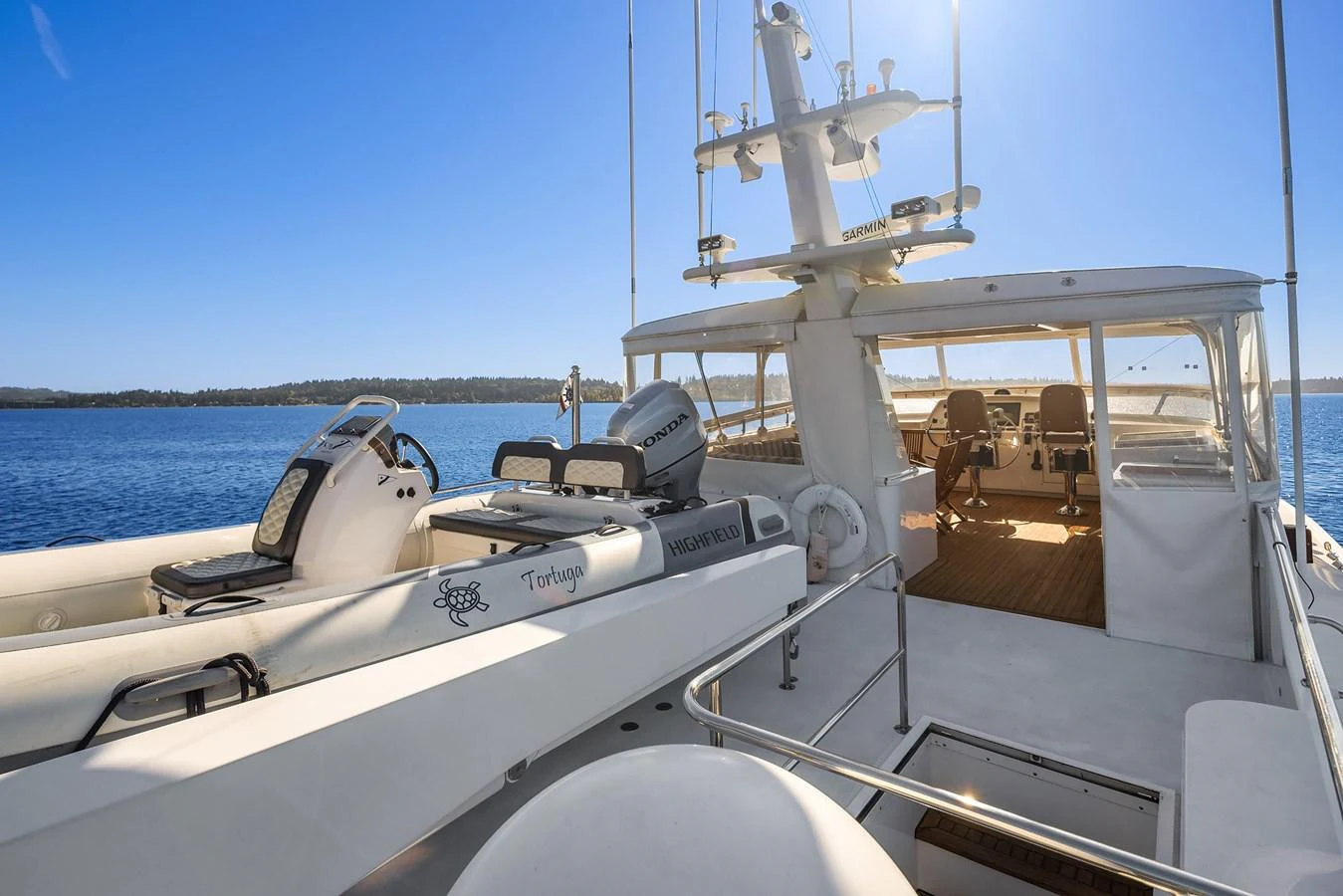 The aft deck of the yacht showcases a spacious and well-equipped area with tenders and seating under a clear blue sky. aboard MI AMERE Yacht for Sale