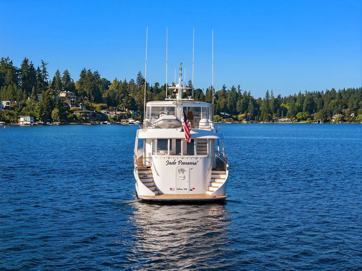 A luxurious yacht is anchored on a serene body of water with a picturesque shoreline in the background. aboard MI AMERE Yacht for Sale