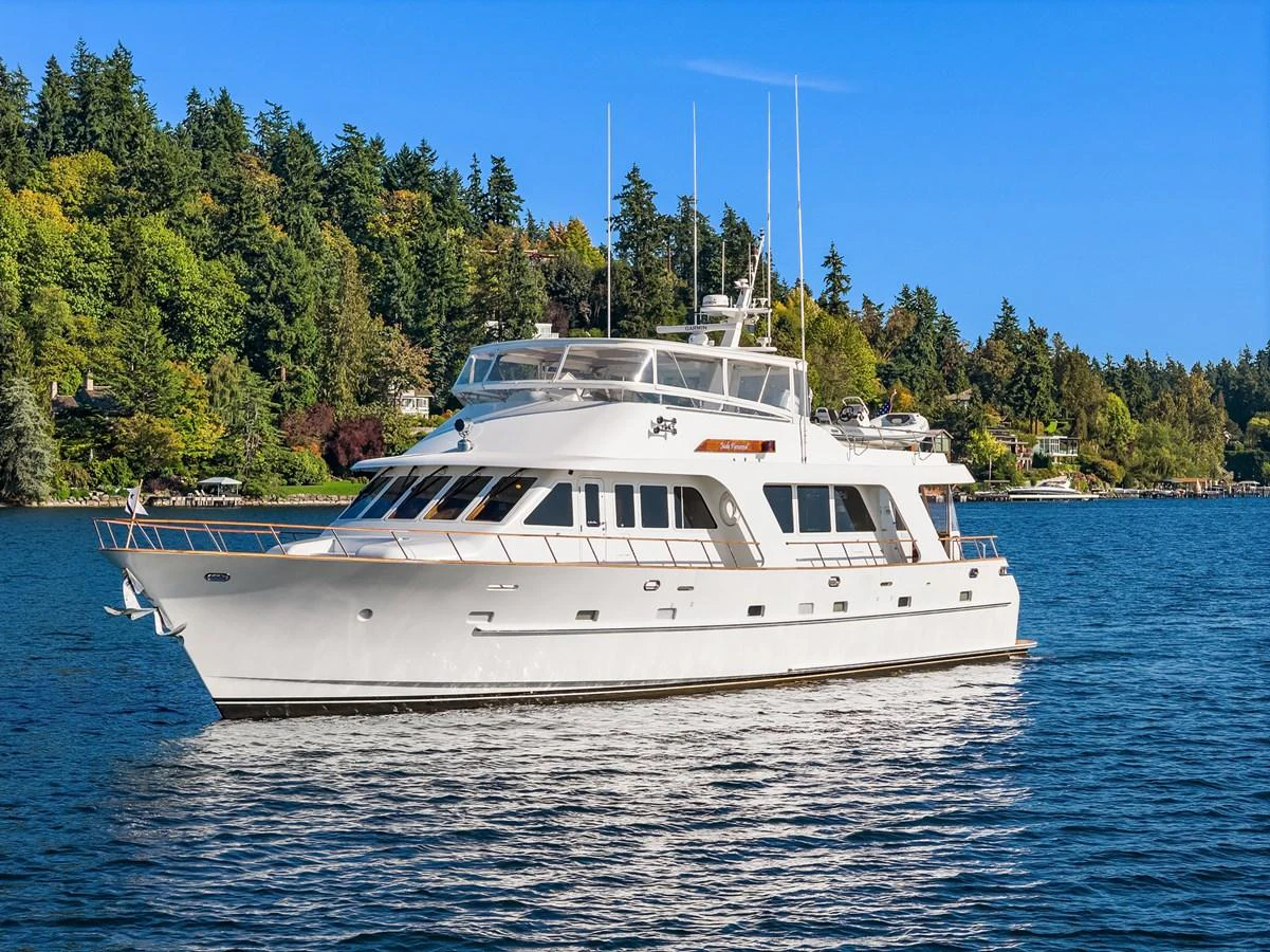 A pristine white yacht cruises gracefully on calm waters against a backdrop of lush greenery. aboard MI AMERE Yacht for Sale