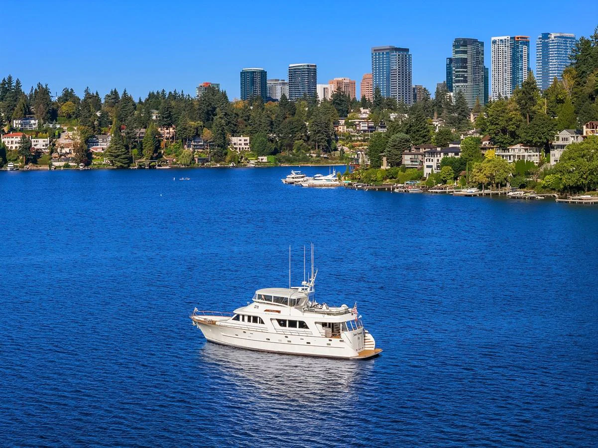 A pristine yacht cruises on a serene blue lake with a cityscape in the background. aboard MI AMERE Yacht for Sale