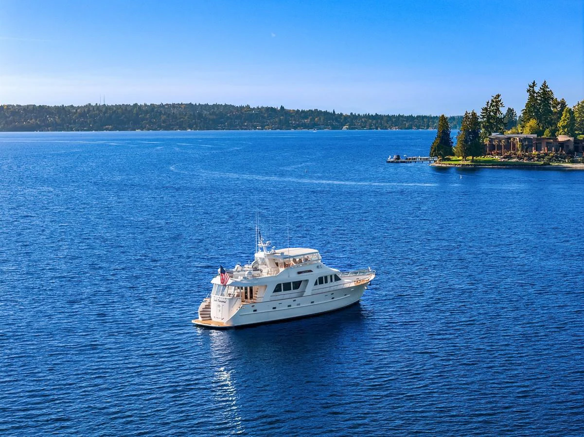 A luxurious yacht cruises peacefully on a serene blue lake with a scenic shoreline in the background. aboard MI AMERE Yacht for Sale