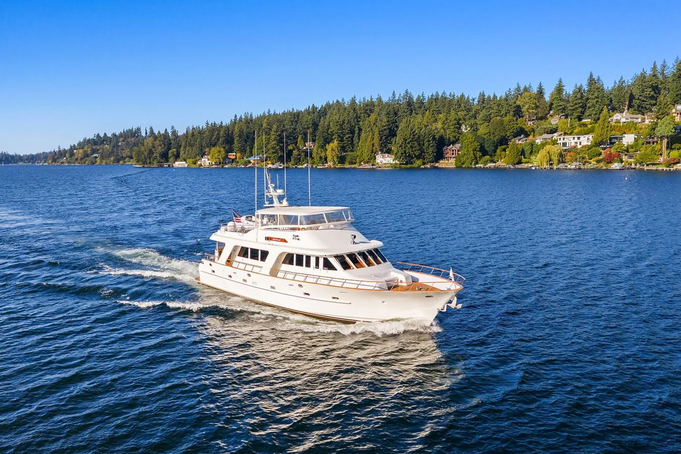 A luxurious yacht cruises gracefully on a serene body of water with a scenic shoreline in the background. aboard MI AMERE Yacht for Sale