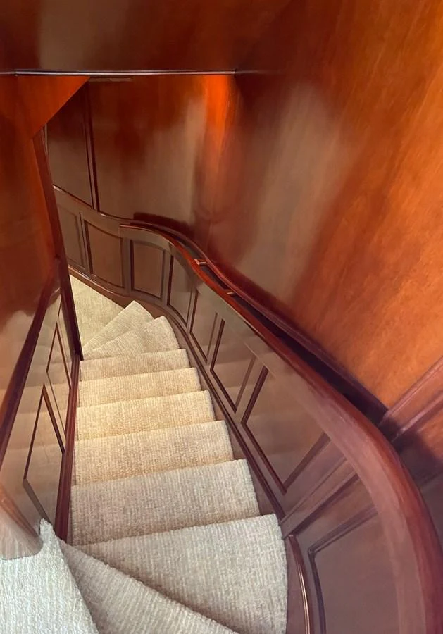 A beautifully crafted wooden staircase with carpeted steps inside the yacht. aboard MI AMERE Yacht for Sale