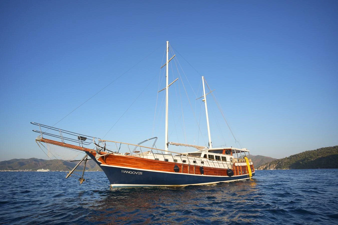 A classic wooden yacht sails gracefully on calm blue waters under a clear sky. aboard HANGOVER Yacht for Sale