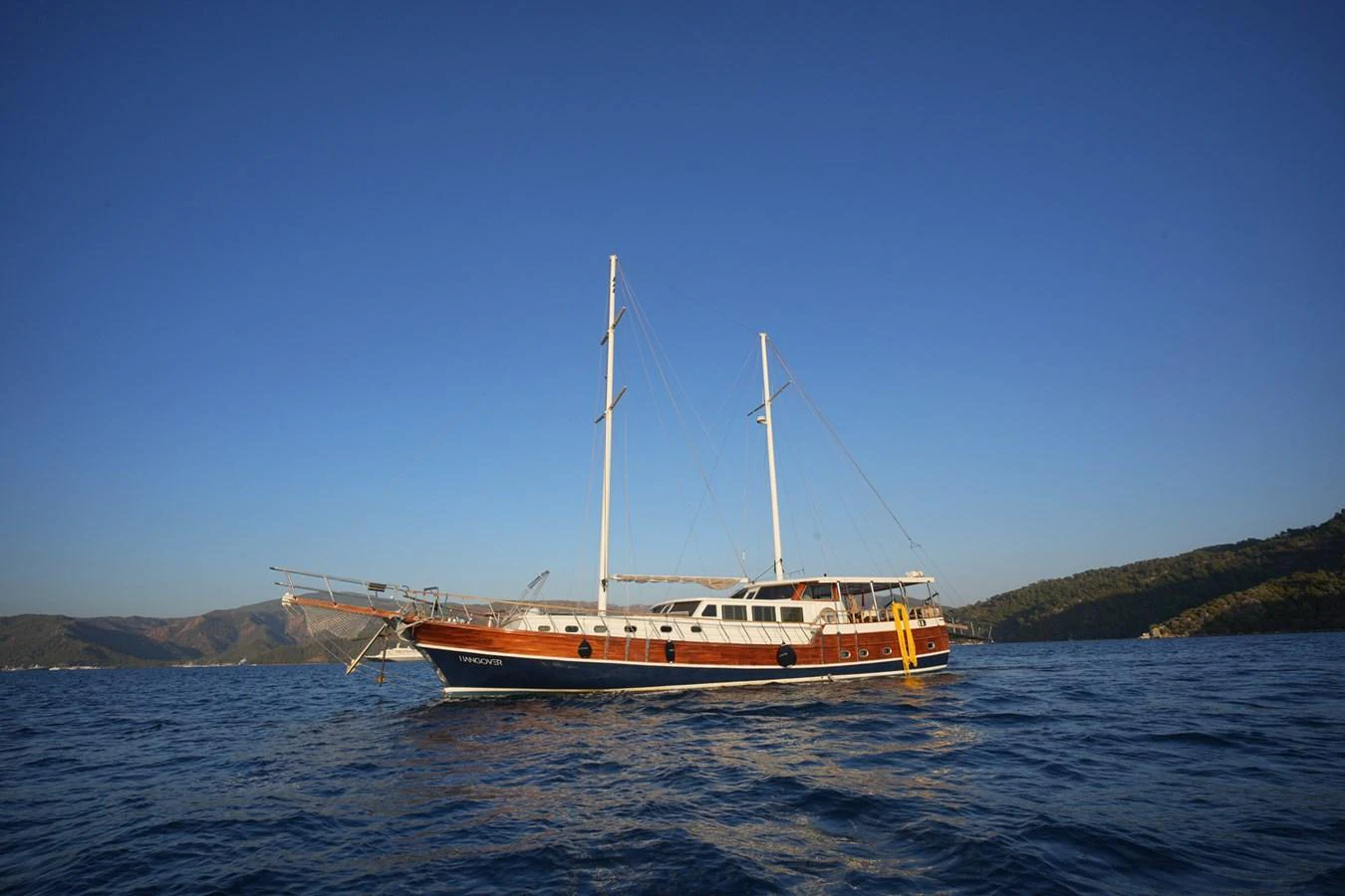 A classic sailing yacht gracefully anchored in calm waters under a clear blue sky. aboard HANGOVER Yacht for Sale