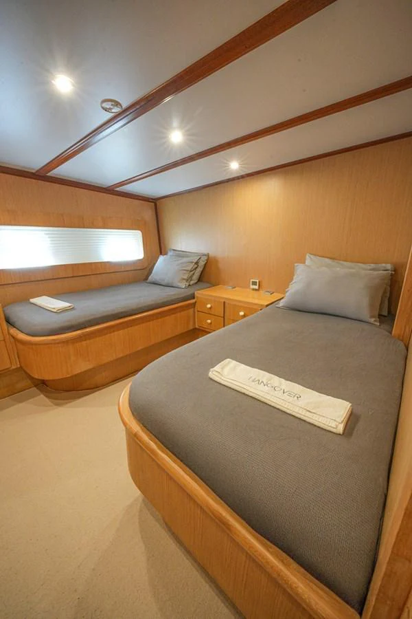 A cozy twin stateroom with wooden accents and comfortable bedding. aboard HANGOVER Yacht for Sale