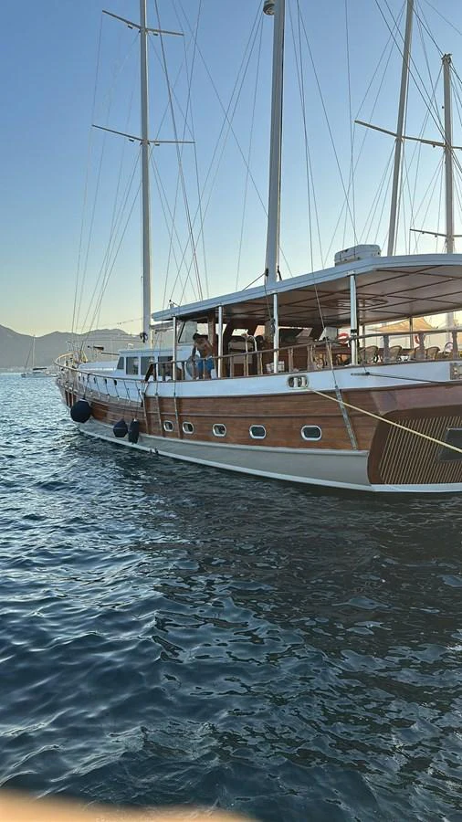 A classic wooden yacht with multiple masts is anchored on calm waters during sunset. aboard HANGOVER Yacht for Sale