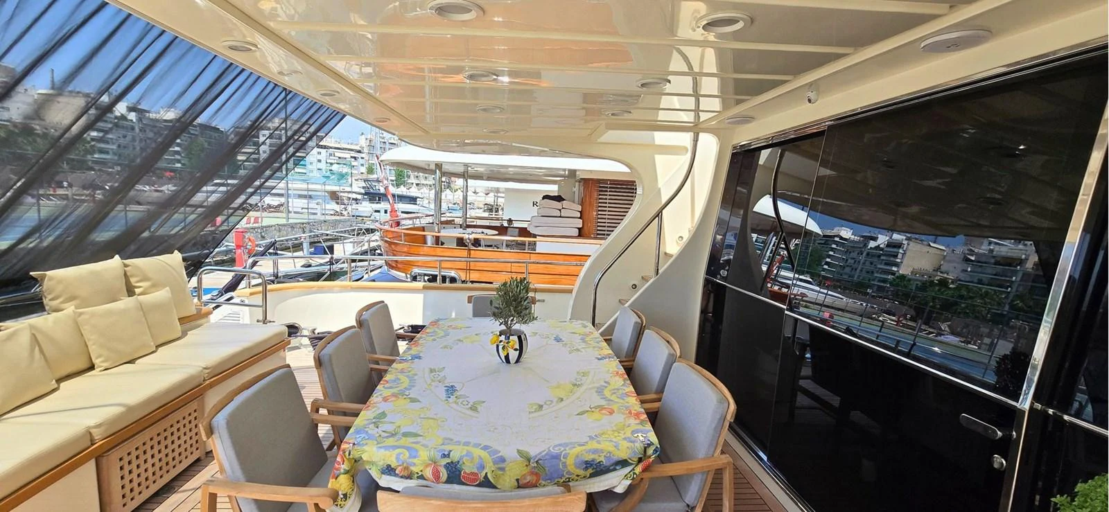 The aft deck features a comfortable dining area with a table set for a meal, surrounded by cushioned seating and a view of the marina. aboard BALKAN Yacht for Sale