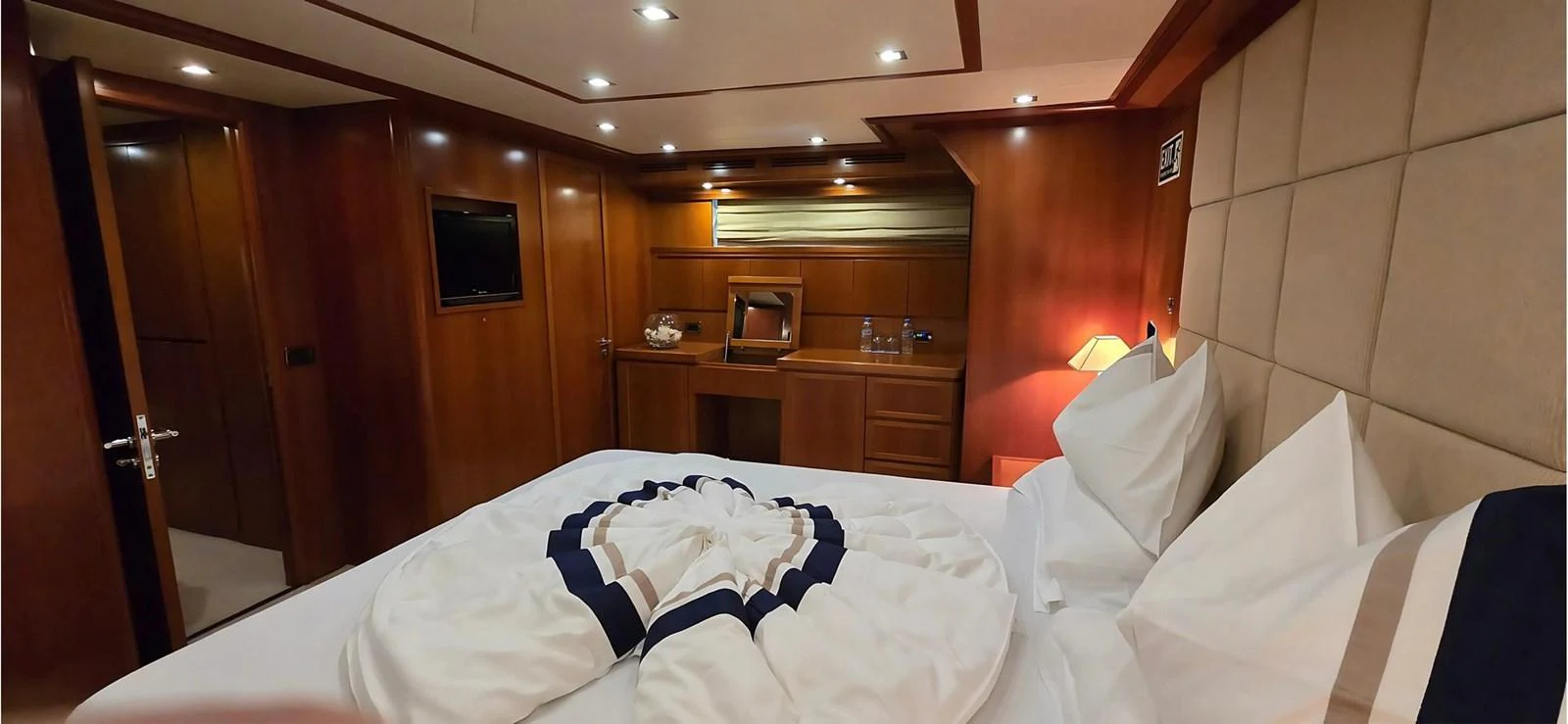 A cozy stateroom featuring warm wooden finishes and a neatly arranged bed with decorative pillows. aboard BALKAN Yacht for Sale