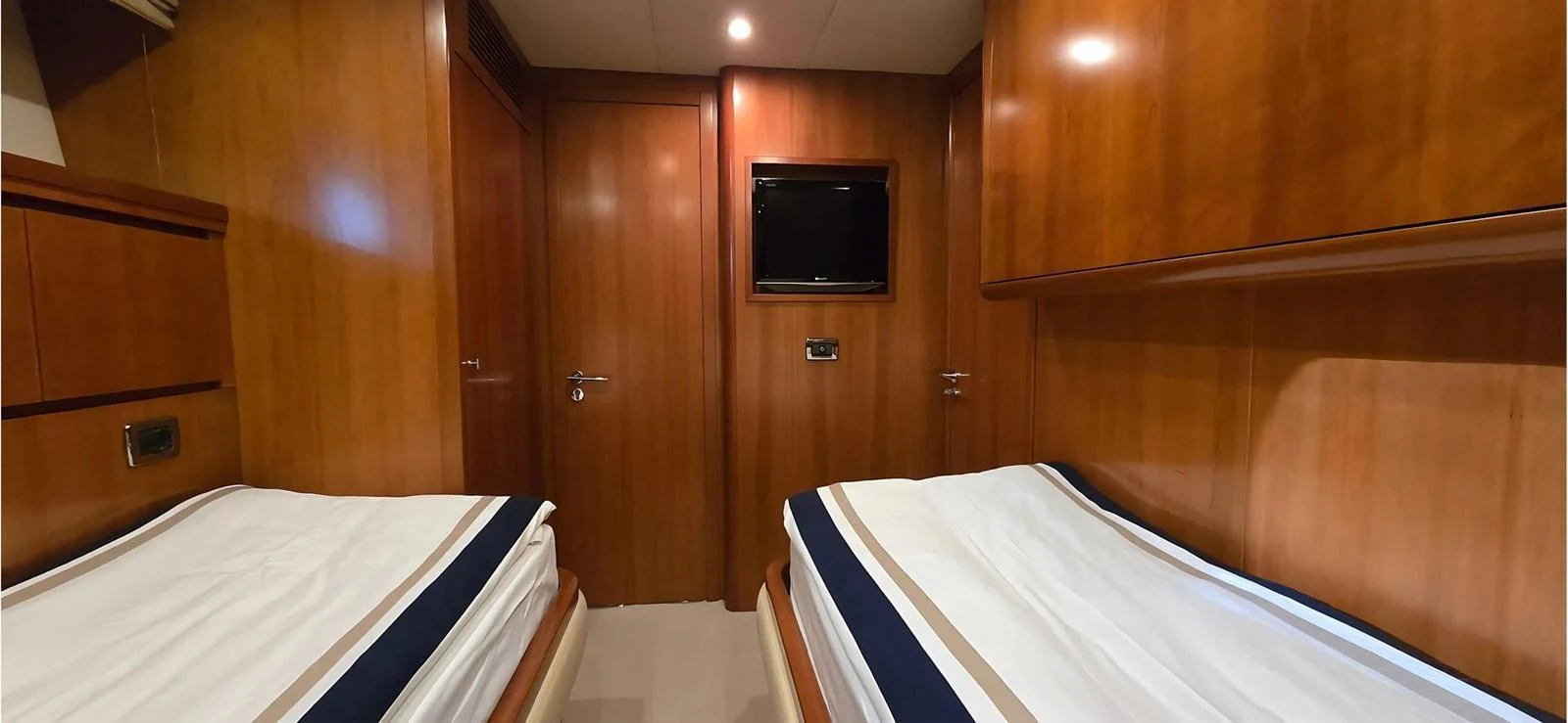 The twin stateroom features two single beds with a warm wood finish and a mounted television. aboard BALKAN Yacht for Sale