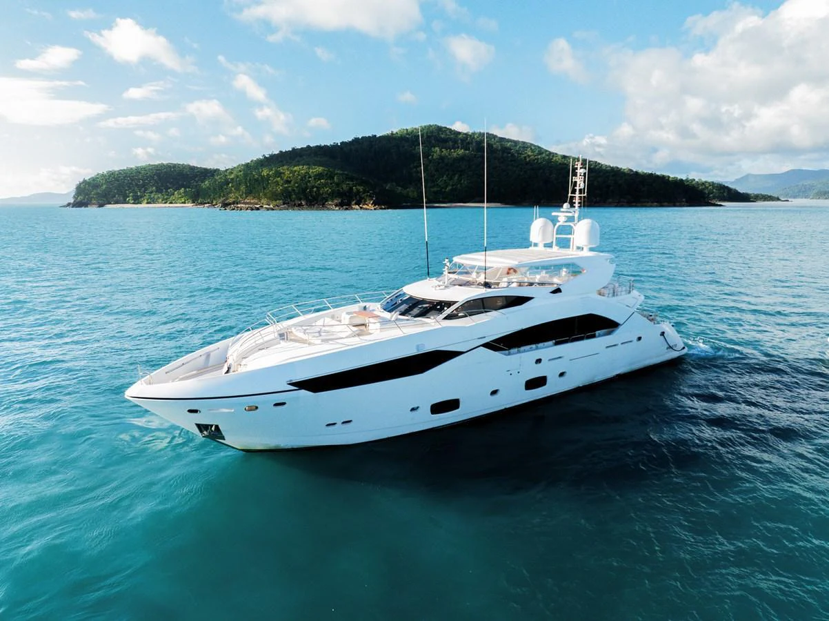 A sleek and modern yacht cruises through clear blue waters with a scenic island backdrop. aboard RASCAL Yacht for Sale