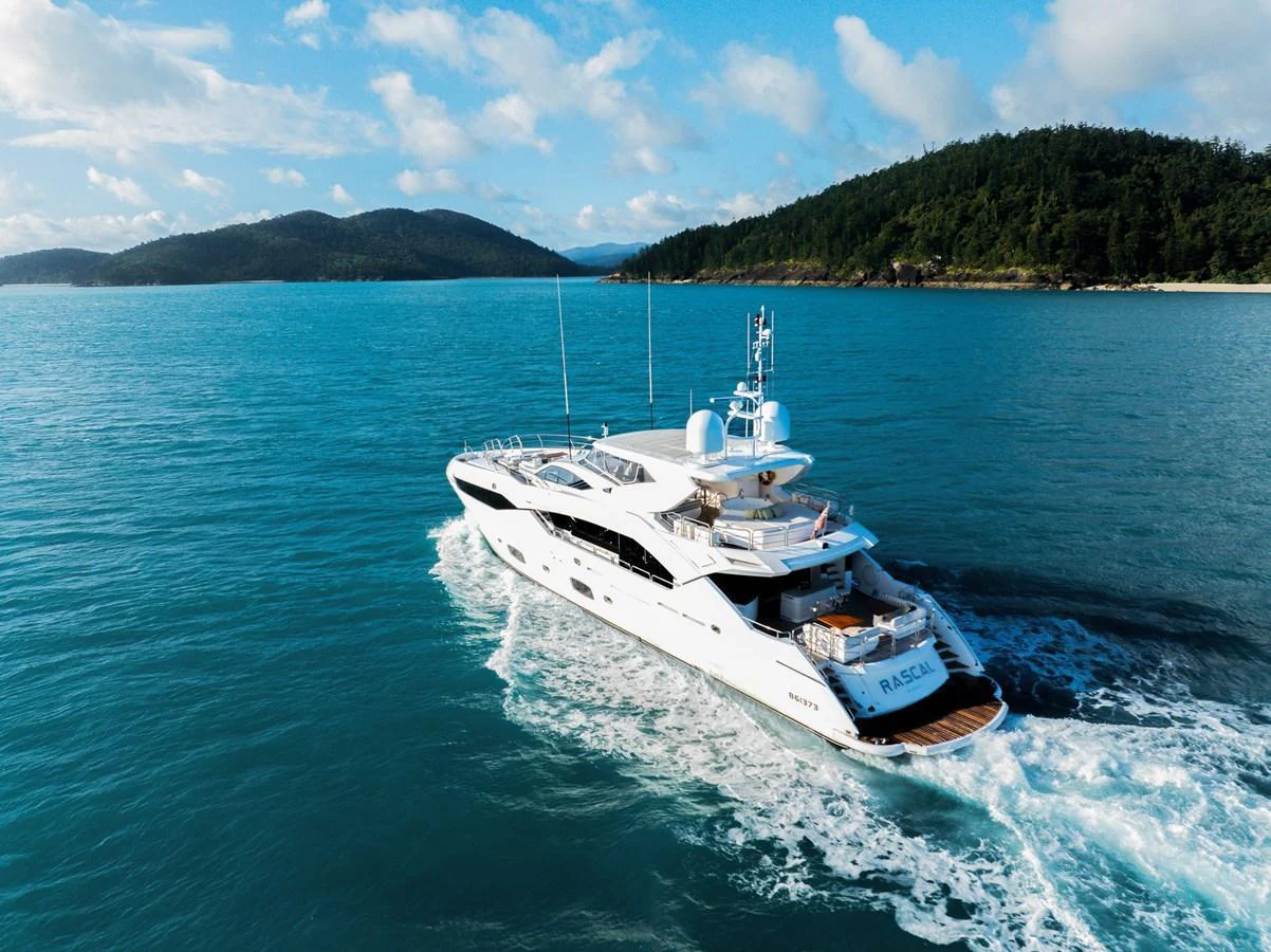 A luxurious yacht cruises through pristine blue waters with scenic hills in the background. aboard RASCAL Yacht for Sale