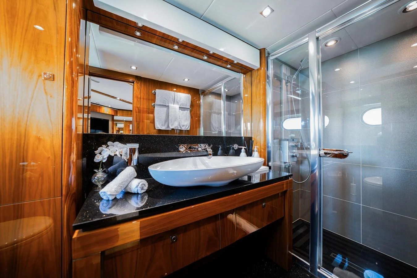The yacht's bathroom features elegant wood paneling, a sleek countertop, and a modern glass shower. aboard RASCAL Yacht for Sale