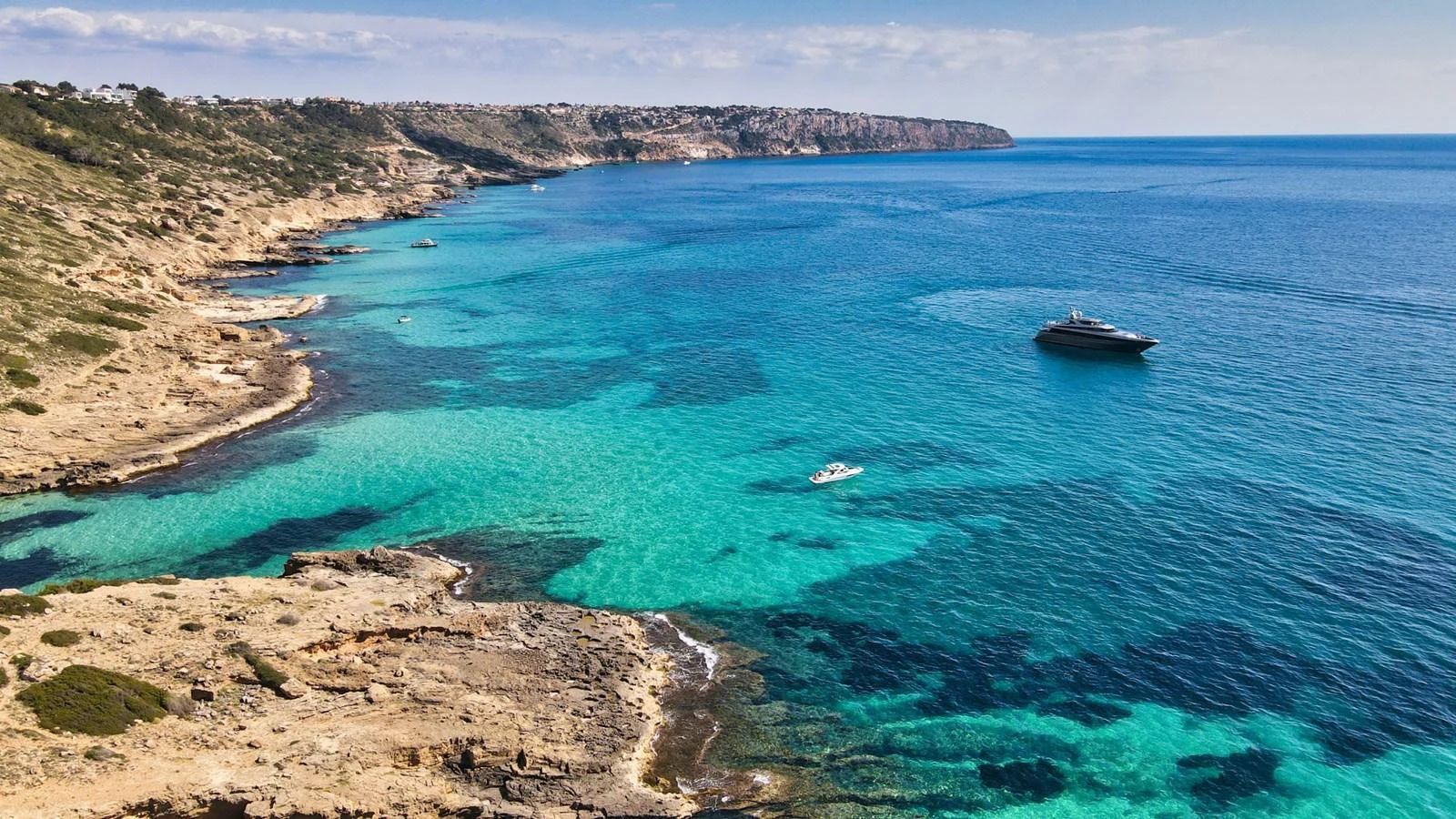 A sleek yacht cruises through crystal-clear turquoise waters along a rugged coastline. aboard SMOOTH OPERATOR Yacht for Sale