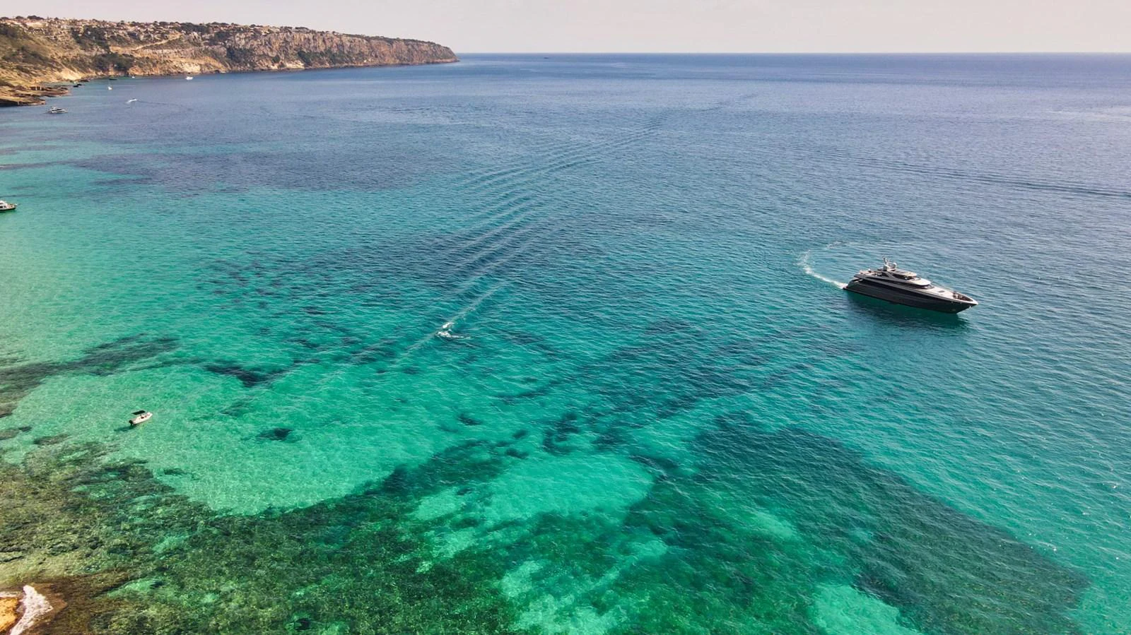 A sleek yacht cruises through crystal-clear turquoise waters near a rugged coastline. aboard SMOOTH OPERATOR Yacht for Sale