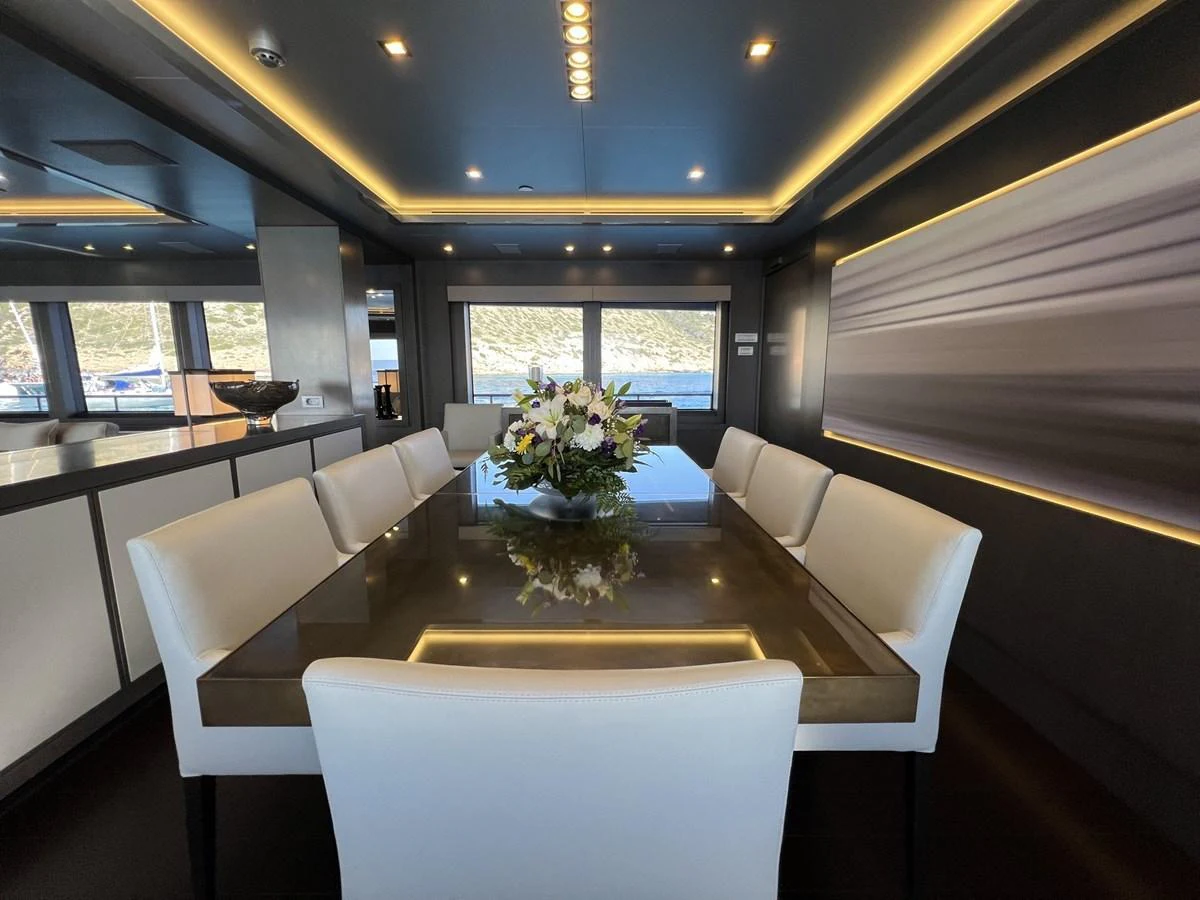 The yacht's dining area features a sleek table surrounded by plush white chairs, with large windows offering scenic views. aboard SMOOTH OPERATOR Yacht for Sale