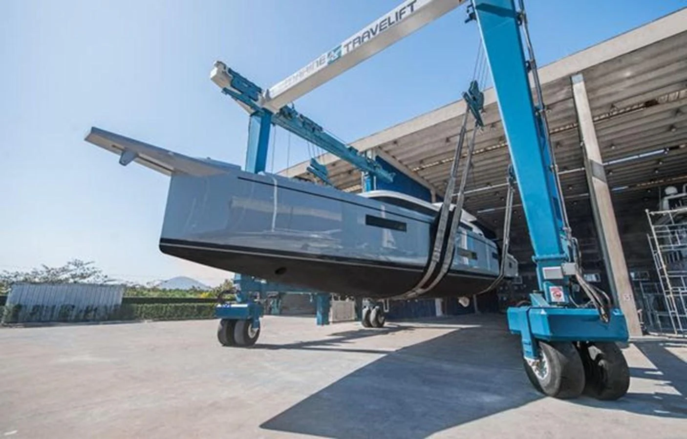 The yacht is being lifted by a large travel lift in a shipyard, showcasing its sleek hull design. aboard 2025 MCP GLOBAL EXP 68 Yacht for Sale