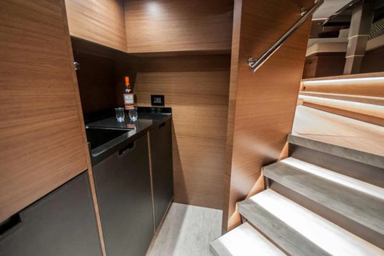 A sleek and modern stairway area with wooden paneling and a small bar setup. aboard 2025 MCP GLOBAL EXP 68 Yacht for Sale