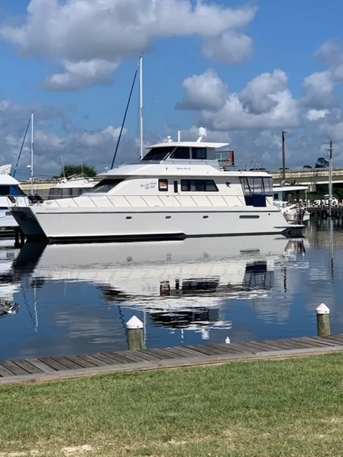 A sleek yacht is docked at a marina, reflecting beautifully on the calm water under a partly cloudy sky. aboard THE CAT FROM THE HAT Yacht for Sale