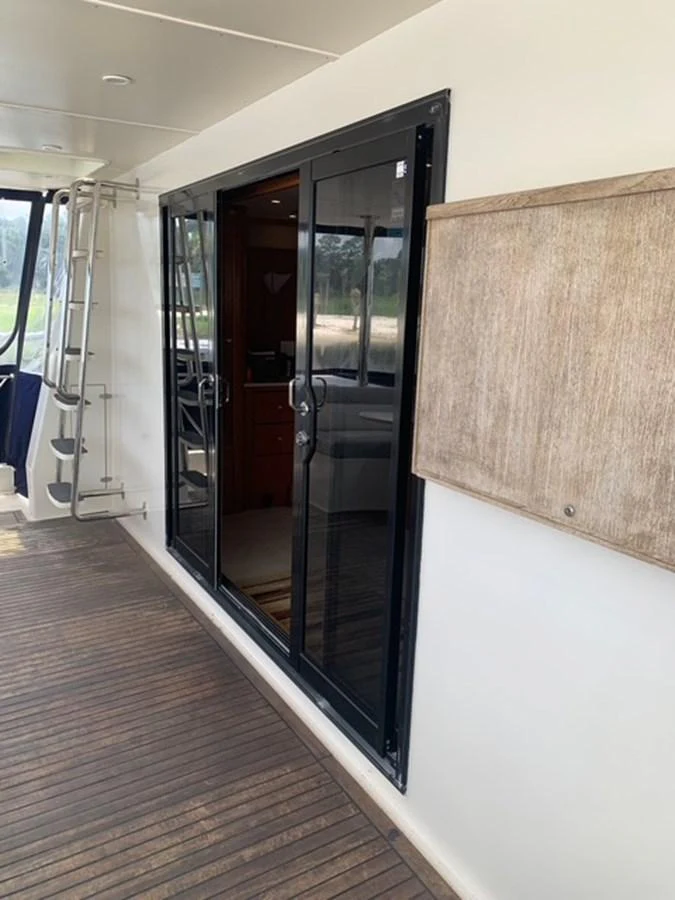 The aft deck features sliding glass doors leading to the interior, with a wooden floor and a ladder visible. aboard THE CAT FROM THE HAT Yacht for Sale