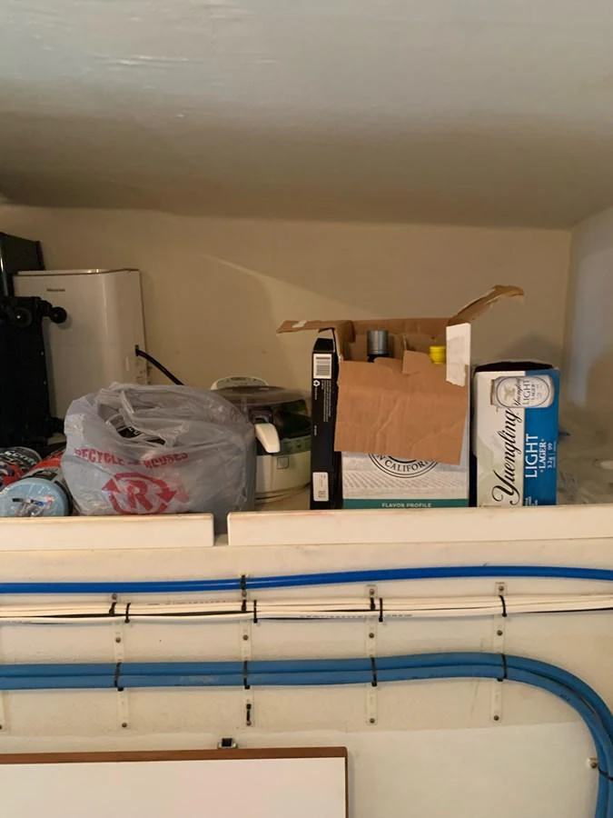 A storage area with various items and supplies, including a box of beer and some bags. aboard THE CAT FROM THE HAT Yacht for Sale