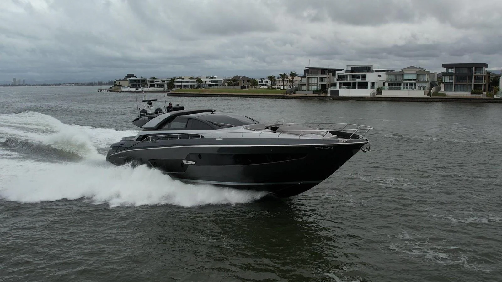 A sleek, modern yacht cruises swiftly through calm waters near a luxurious waterfront community. aboard EVENFLOW Yacht for Sale
