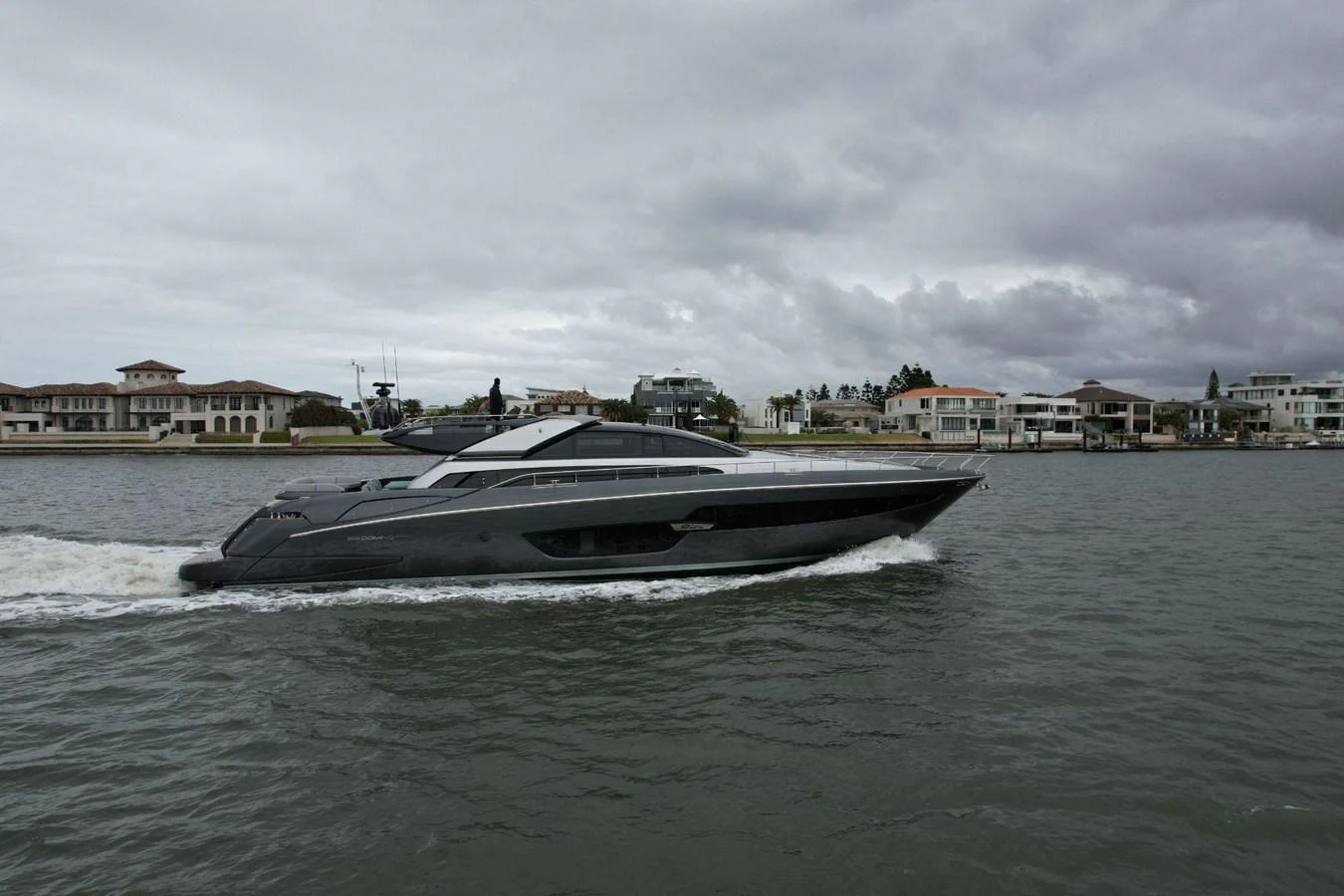 A sleek, modern yacht cruises along the waterfront under a cloudy sky. aboard EVENFLOW Yacht for Sale