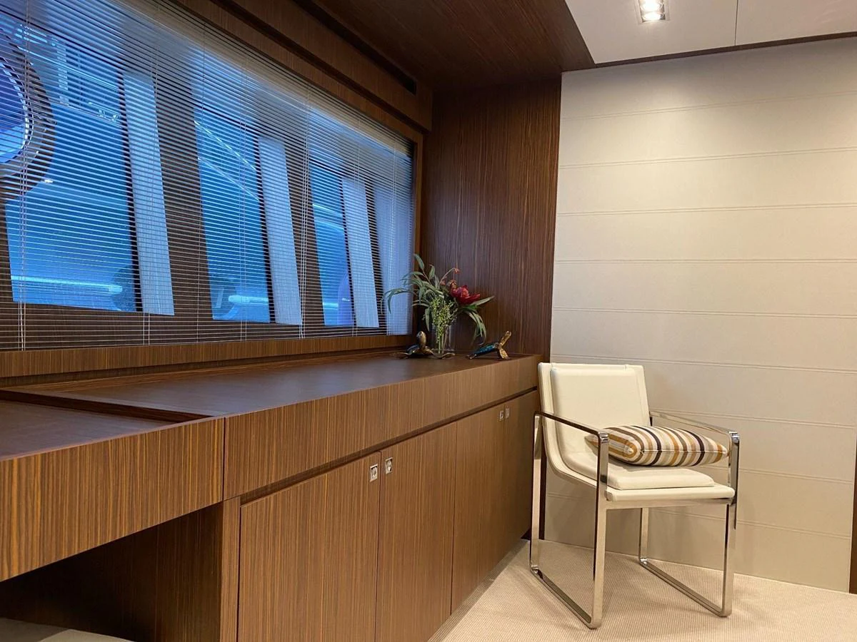 A modern yacht interior featuring a sleek wooden cabinet and a stylish chair with a striped cushion. aboard EVENFLOW Yacht for Sale