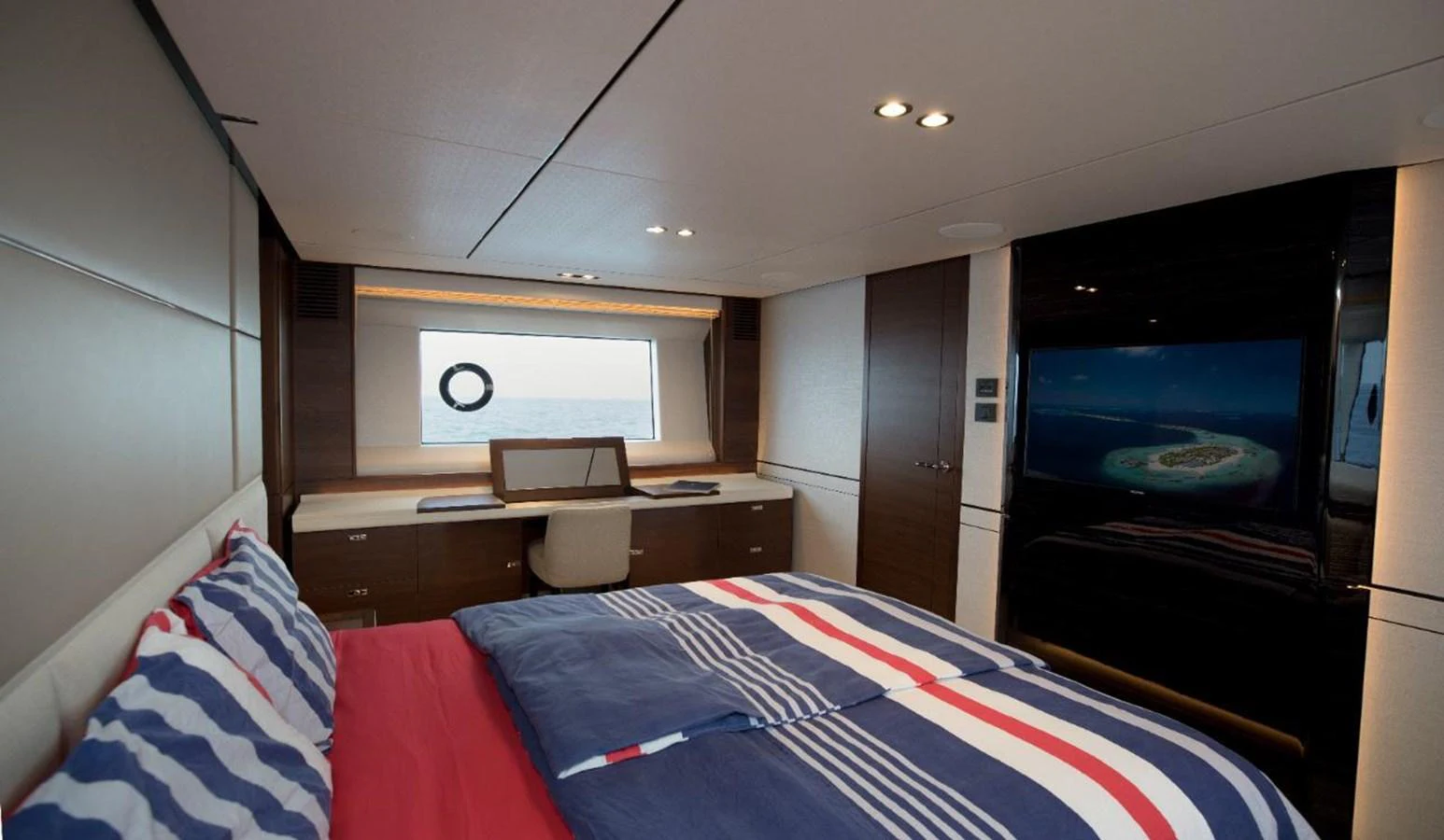 A cozy stateroom with a large bed, desk, and a window offering a view of the sea. aboard RAGARDA Yacht for Sale