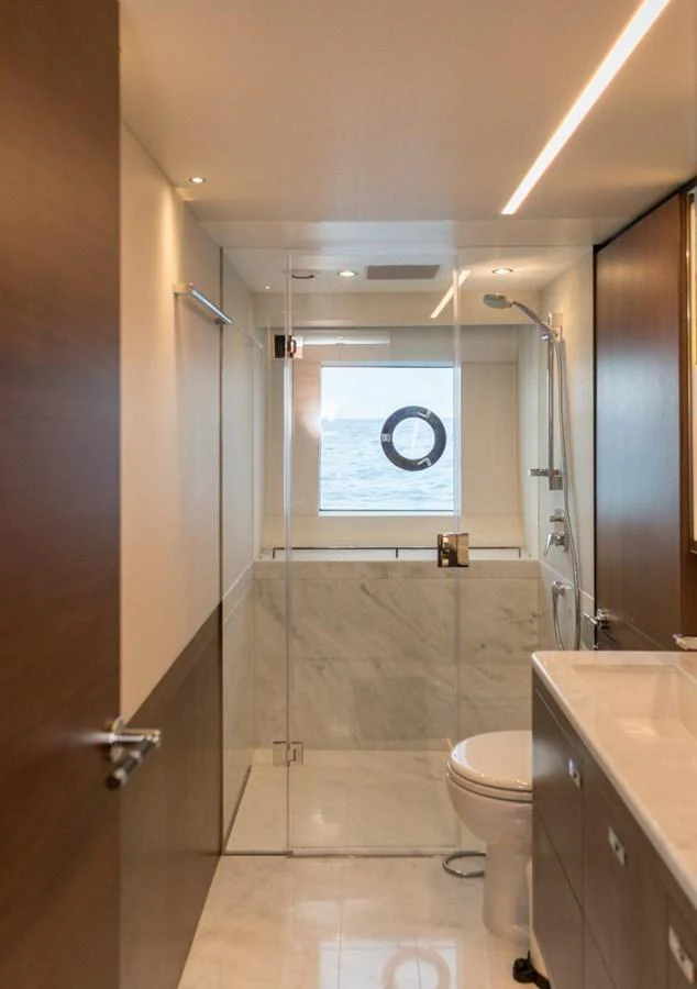 A sleek and modern yacht bathroom with a glass-enclosed shower and a porthole window offering a view of the sea. aboard RAGARDA Yacht for Sale