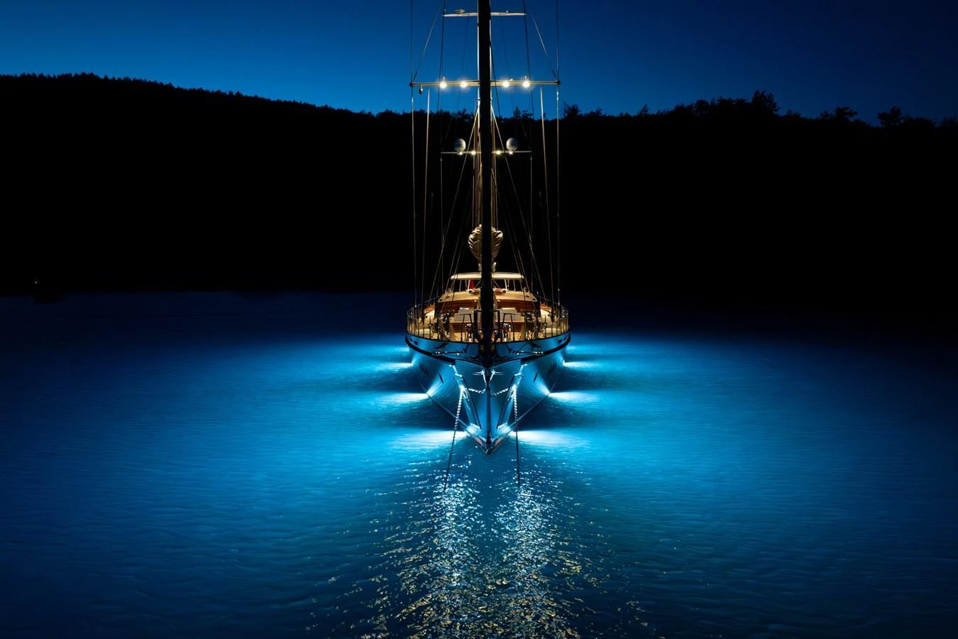 A stunning yacht illuminated by underwater lights, creating a captivating reflection on the water at night. aboard SALLYNA Yacht for Sale