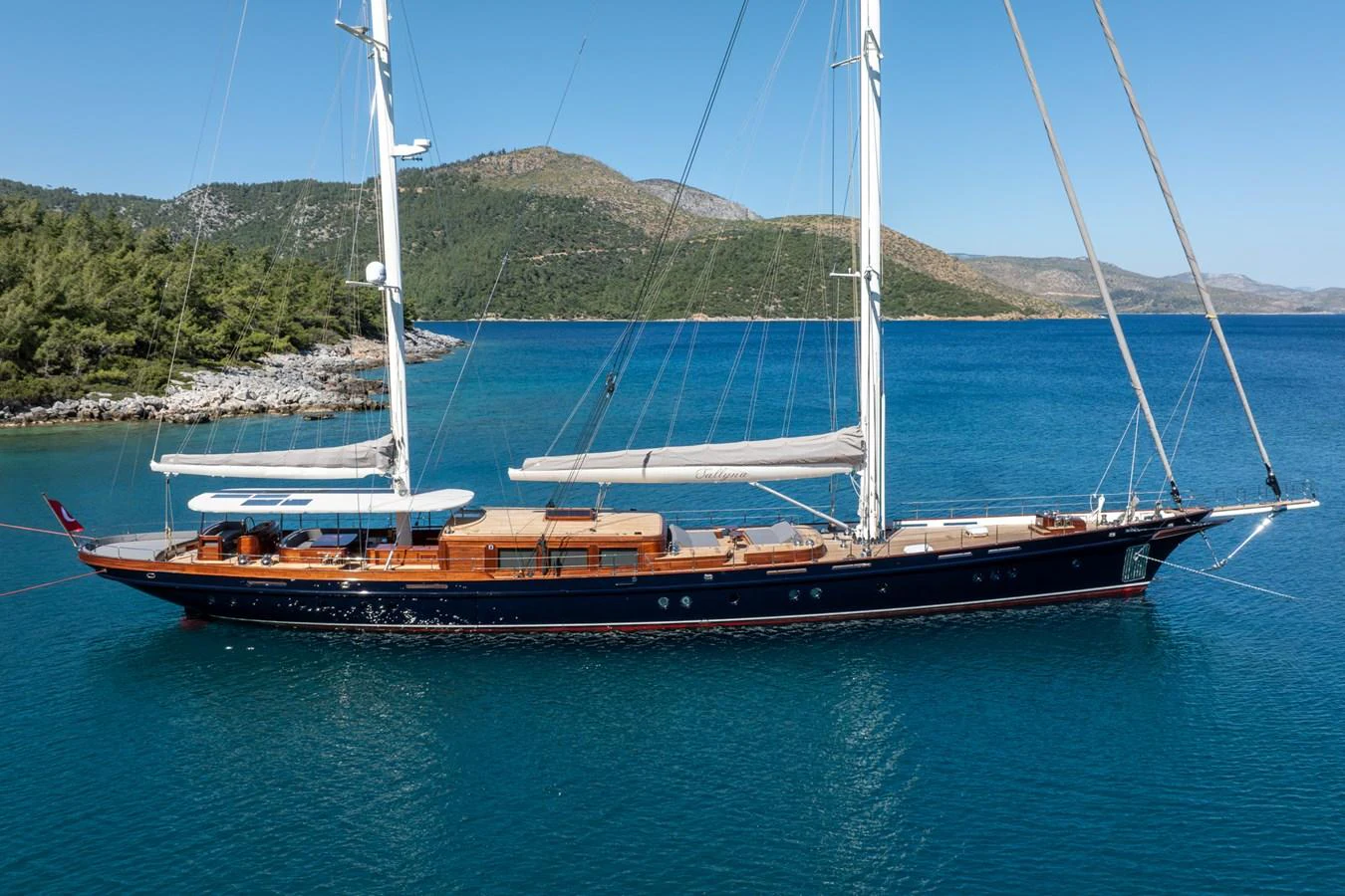 A stunning sailing yacht anchored in a serene bay with clear blue waters and a picturesque backdrop. aboard SALLYNA Yacht for Sale