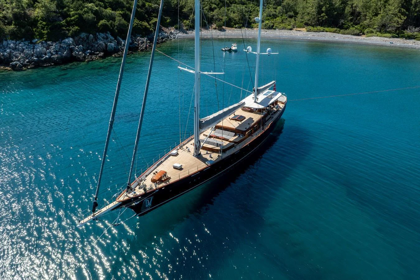 A stunning yacht is anchored in a serene, clear blue bay surrounded by lush greenery. aboard SALLYNA Yacht for Sale